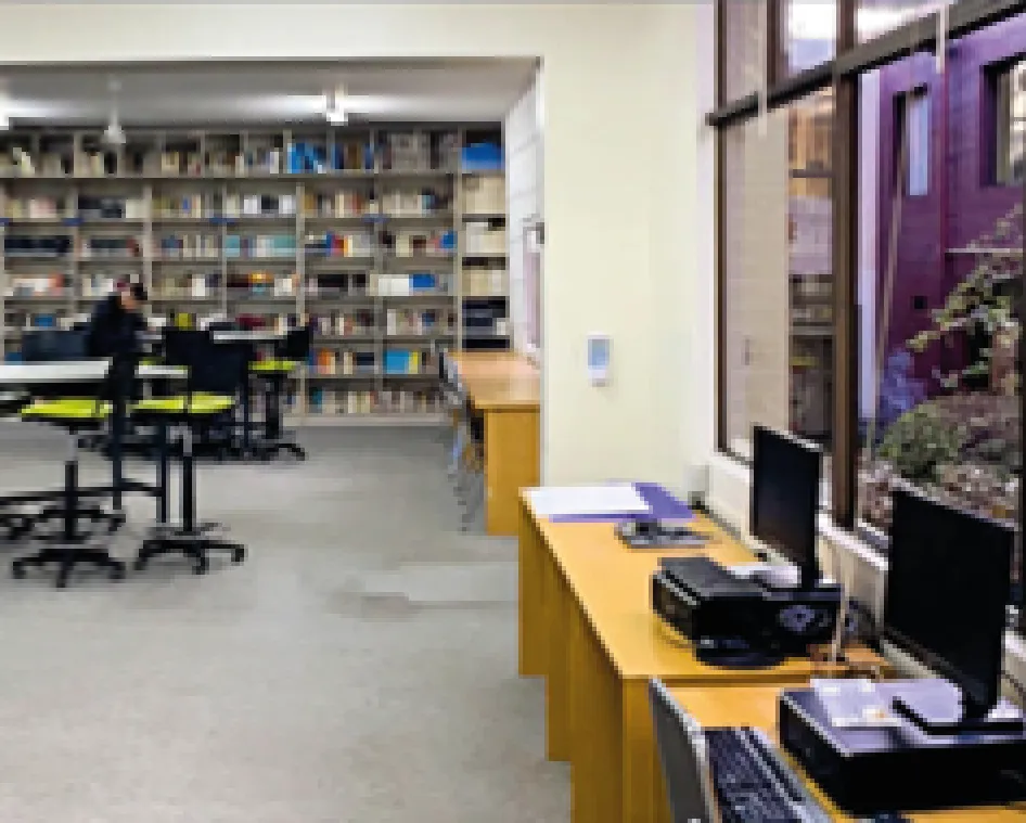 Sala de computación con filas de computadores y estantes con libros al fondo.