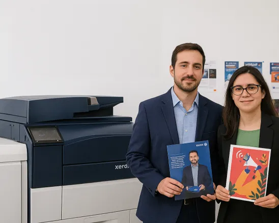 Una mujer y un hombre sonríen junto a una impresora Xerox de alto volumen y sostienen material impreso.