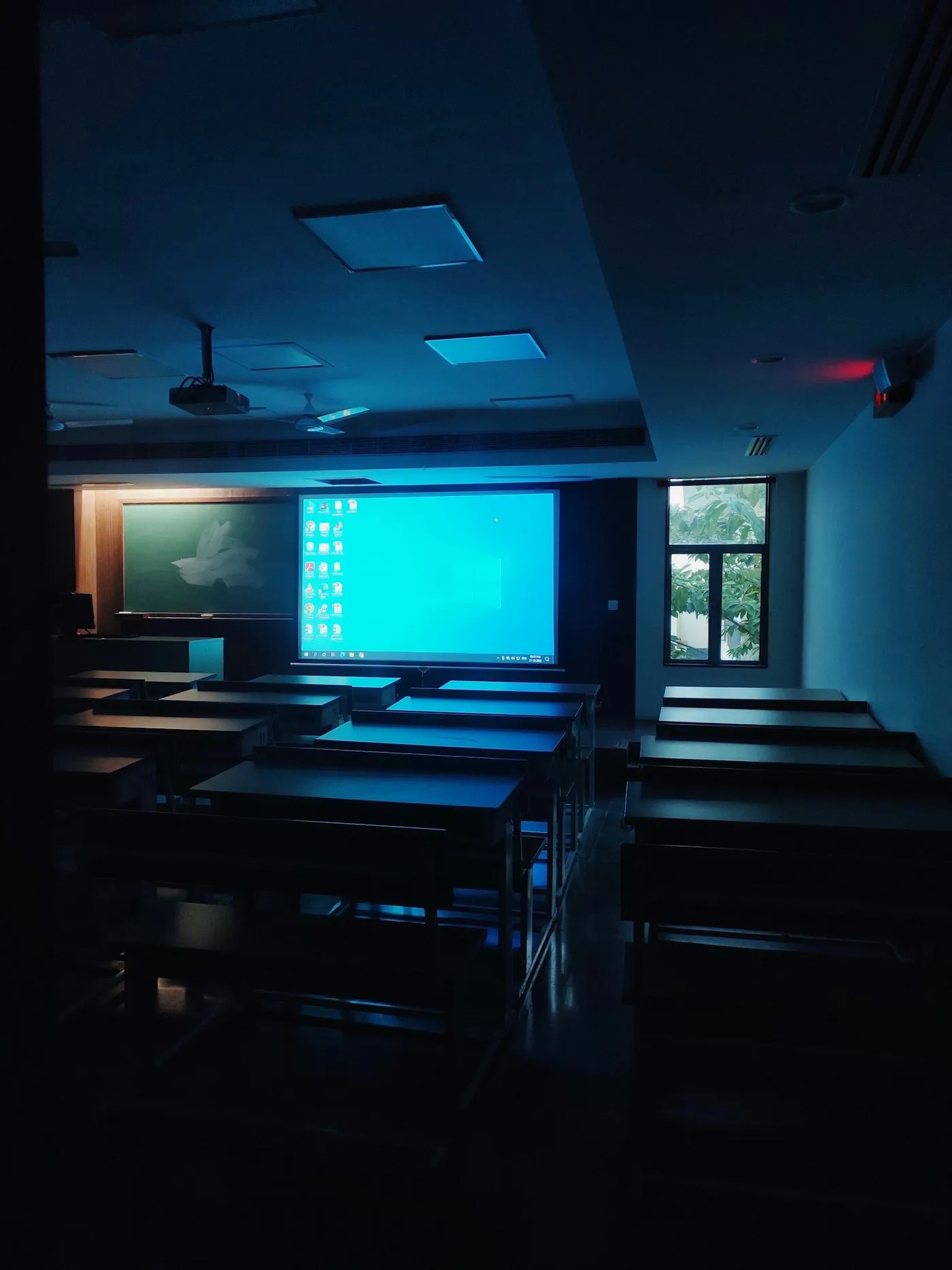 Sala de clases a oscuras con una pantalla encendida al fondo.